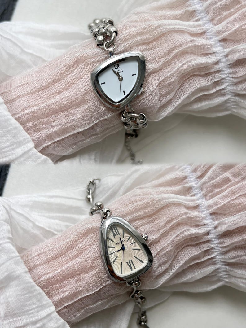 K&ouml;nnte beinhalten: Eine silberne Uhr mit einem dreieckigen Zifferblatt und r&ouml;mischen Ziffern. Die Uhr hat ein silbernes Kettenarmband.