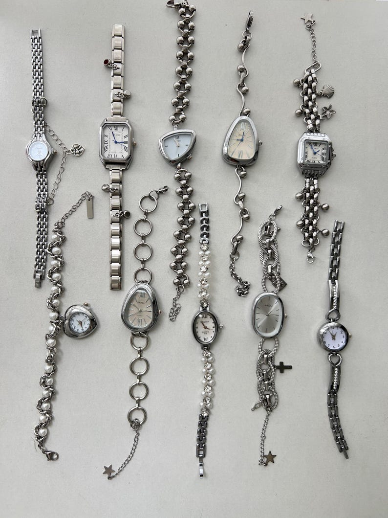 K&ouml;nnte beinhalten: Eine Sammlung von zehn silbernen Armbanduhren mit verschiedenen Band- und Zifferblattstilen. Die Uhren haben verschiedene Charms und Verzierungen, darunter Sterne, Herzen und Muscheln.