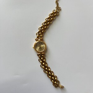 Puede incluir: Un reloj de pulsera dorado con una esfera redonda y una pulsera de eslabones.