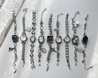 May include: Nine silver-toned wristwatches with various chain and charm designs. The watch faces are in different shapes, including round, oval, and square. Some watches have black faces, while others are white.