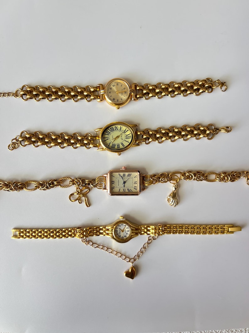 Puede incluir: Cuatro relojes de pulsera de tono dorado con correas de eslabones. Los relojes tienen diferentes estilos de esferas y algunos tienen dijes unidos a las correas.