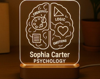 May include: A personalised night light with a brain design, featuring sections labelled "Creativity," "Logic," and "Emotions." The name "Sophia Carter" and the word "Psychology" are displayed below the brain graphic. The light has a wooden base.