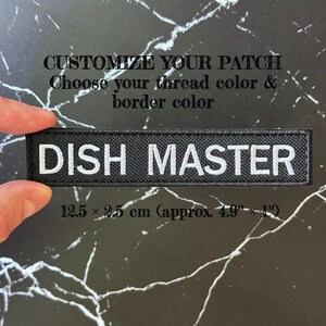 Puede incluir: Un parche rectangular negro bordado con el texto blanco DISH MASTER. El parche mide 12,5 x 2,5 cm. El texto CUSTOMIZE YOUR PATCH Choose your thread color & border color es visible sobre el parche en el fondo oscuro de la imagen.