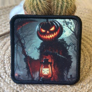 Könnte beinhalten: Quadratischer Aufnäher mit einem Halloween-Design. Das Bild zeigt eine Vogelscheuche mit einem Kürbiskopf, die eine Laterne hält. Der Hintergrund zeigt einen Vollmond und Bäume. Der Aufnäher hat einen schwarzen Rand.