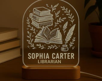 May include: A personalised LED night light with a wooden base. The clear acrylic panel features an engraved design of books, leaves, and a quill. The text reads "SOPHIA CARTER LIBRARIAN".