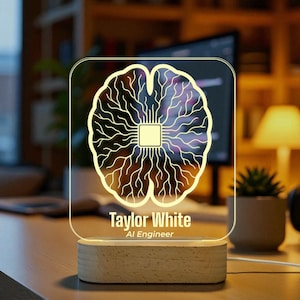Op de afbeelding: Een heldere acryl bureaulamp met een hersenontwerp, een centraal vierkant en vertakte lijnen, gemonteerd op een houten voet. De lamp is gepersonaliseerd met de naam "Taylor White" en de titel "AI Engineer".