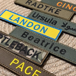 Pode incluir: Close-up de v&aacute;rios patches de nome bordados em v&aacute;rias cores e fontes. Os patches incluem nomes como "Landon", "Beatrice" e "Pace". Os patches est&atilde;o em uma superf&iacute;cie texturizada.