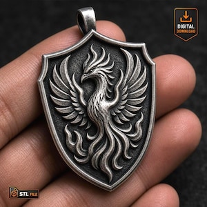 Può includere: Un ciondolo color argento a forma di scudo con un fenice in rilievo, ali spiegate e piume della coda fluenti. Il design presenta uno sfondo scuro e testurizzato con un gancio nella parte superiore. L'immagine include un'icona di download.