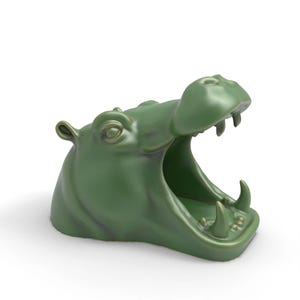 May include: A green ceramic hippo head with an open mouth, showcasing its teeth. The sculpture is a solid, smooth, and glossy finish. The hippo's ears and eyes are detailed. This decorative piece is likely a unique home decor item.
