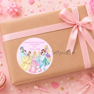 May include: A rectangular gift box wrapped in brown paper with a light pink ribbon tied in a bow. A circular sticker on the box features illustrations of seven princesses and the text: THANK YOU FOR COMING TO MY PARTY LOVE Ava-May.