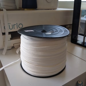 May include: A white elastic band spool on a black plastic base. The spool is full of white elastic band.