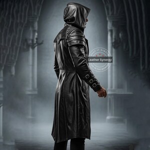May include: A long, black leather hooded coat with shoulder accents and buckle details on the sleeves. The coat has a tailored fit and a flowing skirt. The image shows the coat from the side, highlighting its design and texture. The coat is part of the Leather Synergy collection.