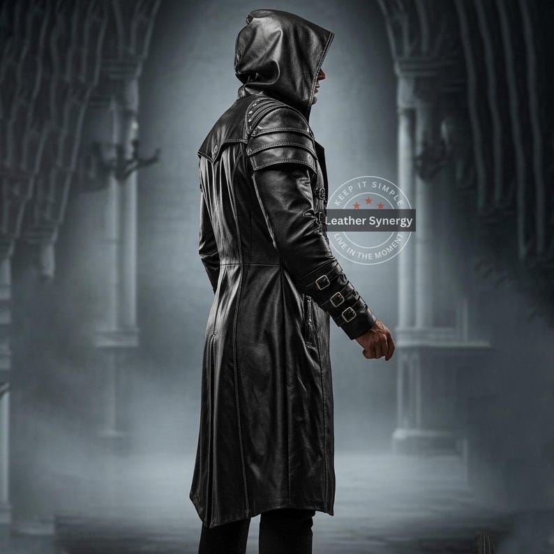 May include: A long, black leather hooded coat with shoulder accents and buckle details on the sleeves. The coat has a tailored fit and a flowing skirt. The image shows the coat from the side, highlighting its design and texture. The coat is part of the Leather Synergy collection.