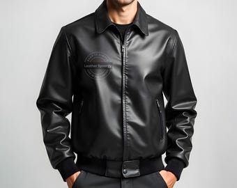 May include: Black leather jacket with a collared neckline, zip-up front, and side pockets. The jacket has a ribbed hem and cuffs. The text "Leather Synergy" is printed on the upper left chest area. A classic outerwear piece.