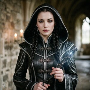 May include: A black leather hooded jacket with silver trim and decorative clasps. The jacket features intricate stitching and shoulder accents. The person in the image has long, dark braided hair and is holding a staff with a glowing tip. The background is a stone hallway.