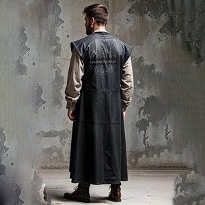 May include: A long, black leather vest with a sleeveless design. The vest features a high collar and a long, flowing skirt. The back of the vest has a circular logo that reads "Leather Synergy". The person is wearing brown boots.