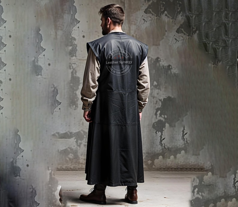 May include: A long, black leather vest with a sleeveless design. The vest features a high collar and a long, flowing skirt. The back of the vest has a circular logo that reads "Leather Synergy". The person is wearing brown boots.