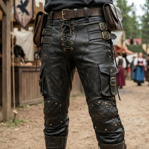 May include: Black leather pants with lace-up front, pockets, and quilted knee patches. The pants feature a brown leather belt with a buckle and two small pouches. The style is reminiscent of medieval or fantasy attire.
