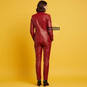 Op de afbeelding: Een persoon is van achteren te zien en draagt een bijpassend rood leren pak. Het pak bestaat uit een blazer en een broek. De achtergrond is effen geel. De blazer heeft een klassiek ontwerp en de broek is getailleerd. De persoon draagt zwarte schoenen.
