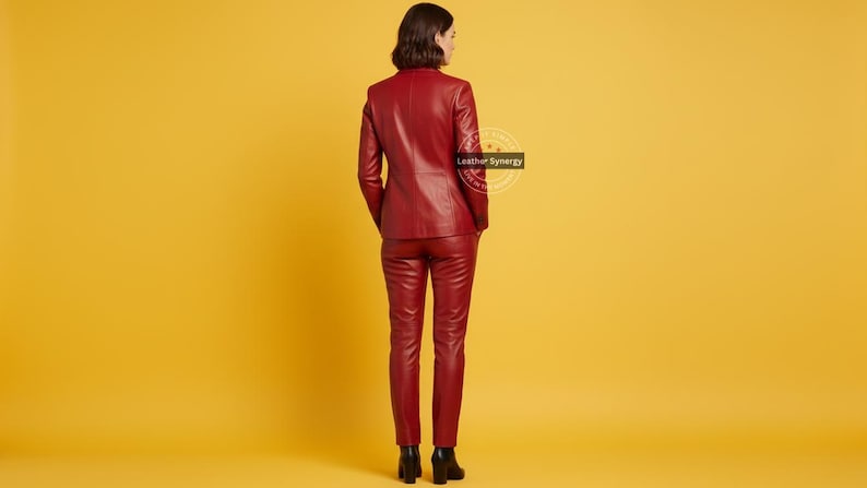 Op de afbeelding: Een persoon is van achteren te zien en draagt een bijpassend rood leren pak. Het pak bestaat uit een blazer en een broek. De achtergrond is effen geel. De blazer heeft een klassiek ontwerp en de broek is getailleerd. De persoon draagt zwarte schoenen.