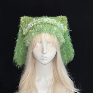 Pode incluir: Uma faixa de cabeça verde com orelhas de gato com um design fofo e texturizado. A faixa de cabeça apresenta uma mistura de detalhes em verde claro, azul e branco. As orelhas estão em pé e a faixa de cabeça está em um fundo preto.