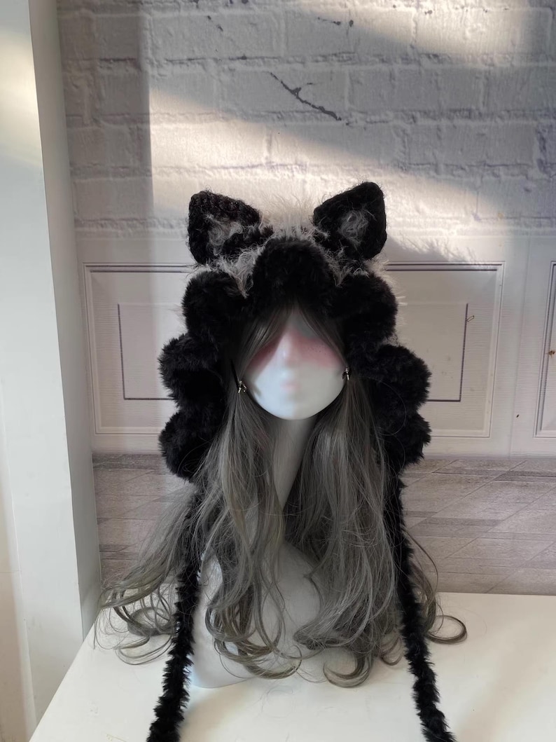 May include: Black faux fur hooded hat with long tails. The hat has cat ears and a fluffy texture.