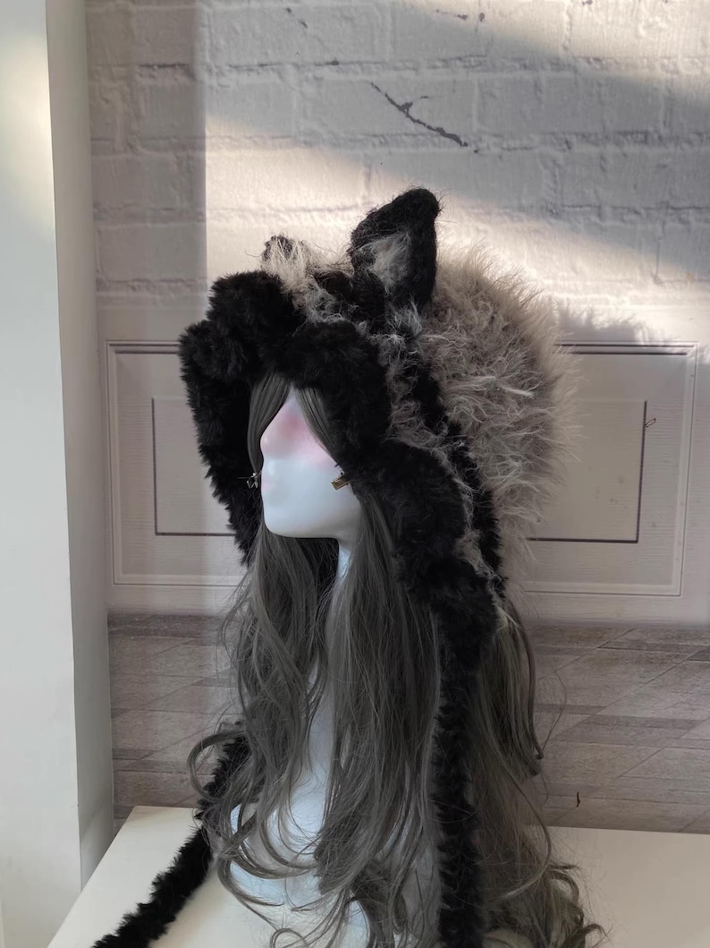 May include: A black and gray faux fur hooded hat with long, dangling fur tails. The hat has two furry ears on top.