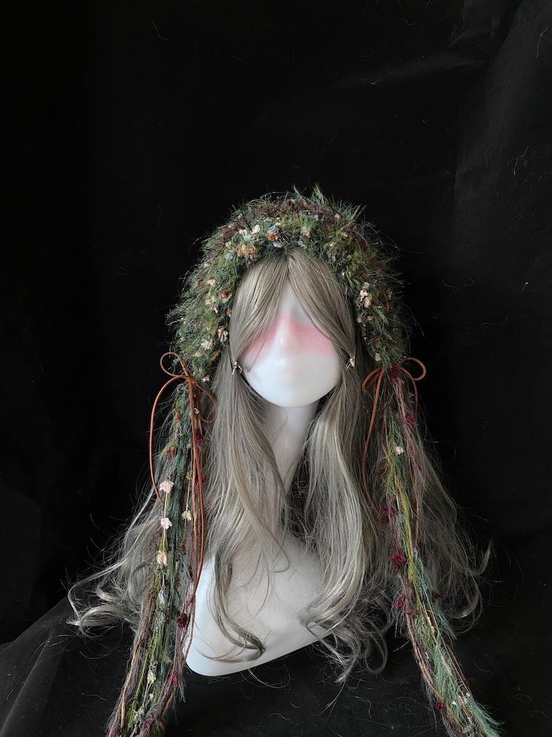 May include: A wig with long, gray hair and a decorative headpiece. The headpiece is made of green and brown materials with small flowers and accents. Brown ribbons and strands of the headpiece hang down the sides.