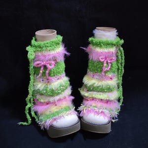 May include: A pair of colorful leg warmers with white platform shoes. The leg warmers are green, pink, and yellow with a fluffy texture and a pink bow. The shoes have a brown sole.
