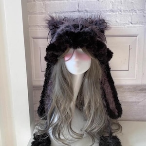 May include: A black and gray fuzzy hat with long ears and black pom-poms. The hat is made of soft, plush fabric and has a cute, whimsical design.