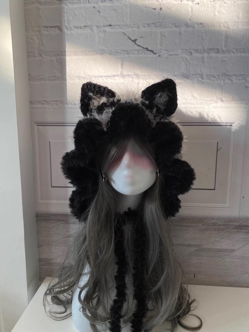 May include: A black and white furry hooded hat with cat ears. The hat has a long black fur tie.