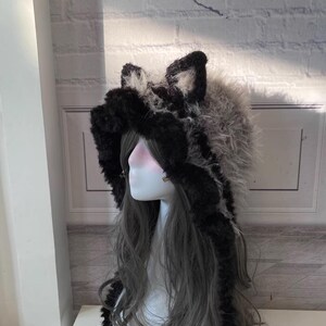 May include: A black and white faux fur hooded hat with long, dangling ear flaps. The hat has a fluffy texture and is designed to resemble a wolf.