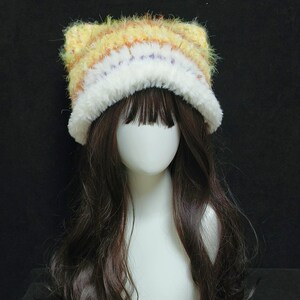 May include: A handmade cat ear hat with a fluffy, textured design. The hat features a mix of yellow, orange, and white yarn, with a white fluffy trim. The hat is displayed on a mannequin head with long, dark brown hair.