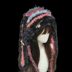 Peut inclure: Un chapeau en fausse fourrure noire avec des accents colorés de rose, bleu et orange. Le chapeau a de longs rabats d'oreilles avec des pompons blancs et un petit charme doré. Le chapeau est conçu pour être porté sur la tête.