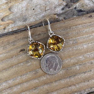 May include: A pair of silver dangle earrings with a square-shaped amber gemstone. The earrings are about the size of a dime.