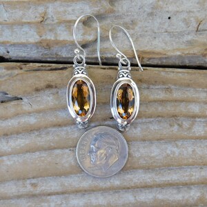 May include: A pair of silver dangle earrings with oval-shaped topaz gemstones. The earrings are approximately the size of a dime.