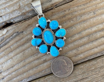 May include: A silver pendant with a cluster of turquoise stones in a flower shape. The pendant is about the size of a US quarter.
