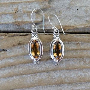 May include: A pair of silver dangle earrings with oval-shaped topaz gemstones. The earrings have a detailed design with a silver filigree around the gemstones.