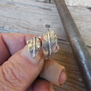 May include: A silver ring with two feather designs. The ring is adjustable and can be worn on any finger.