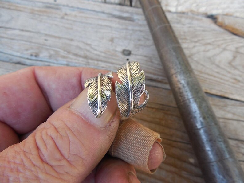 May include: A silver ring with two feather designs. The ring is adjustable and can be worn on any finger.