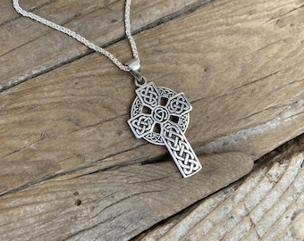 Puede incluir: Un collar con un colgante de cruz celta de plata en una cadena de plata. La cruz está intrincadamente detallada con un diseño de nudo.