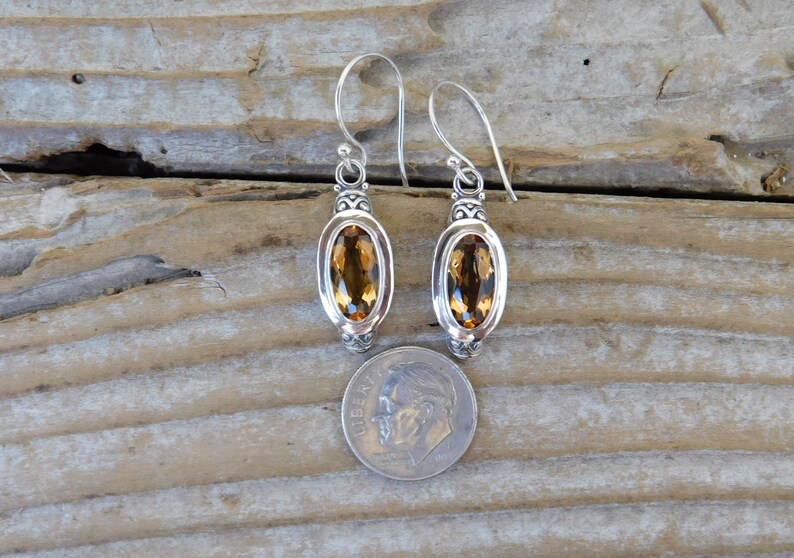 May include: A pair of silver dangle earrings with oval-shaped topaz gemstones. The earrings are about the size of a US dime.