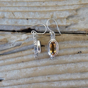 May include: A pair of silver earrings with a detailed filigree design. Each earring features a teardrop-shaped gemstone, one is a dark brown color and the other is a light amber color.