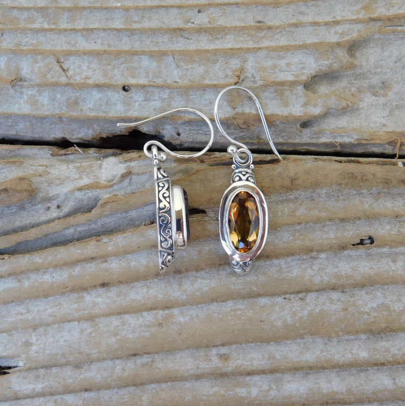 May include: A pair of silver earrings with a detailed filigree design. Each earring features a teardrop-shaped gemstone, one is a dark brown color and the other is a light amber color.
