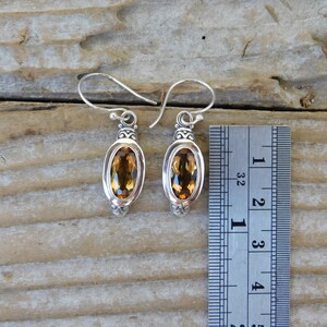 May include: Silver earrings with oval-shaped topaz gemstones. The earrings are approximately 1 1/2 inches long.