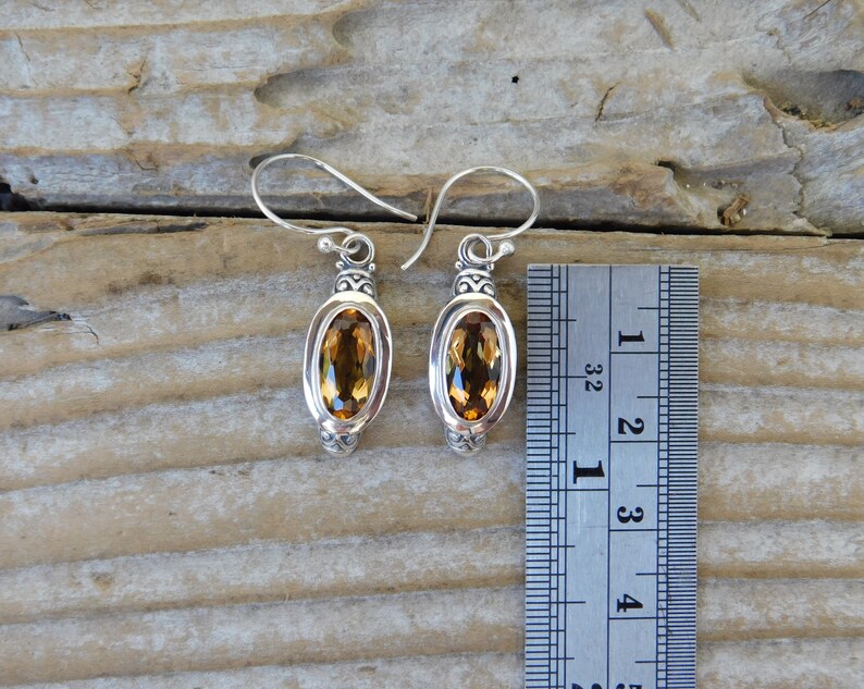 May include: Silver earrings with oval-shaped topaz gemstones. The earrings are approximately 1 1/2 inches long.