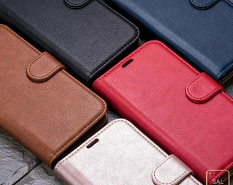 Könnte beinhalten: Eine Sammlung von fünf rechteckigen Handyhüllen im Brieftaschen-Stil mit strukturierter Oberfläche und magnetischen Verschlusslaschen. Die Hüllen sind in Schwarz, Marineblau, Braun, Rot und Metallic-Rosa erhältlich, mit dem Text SAL CASES.