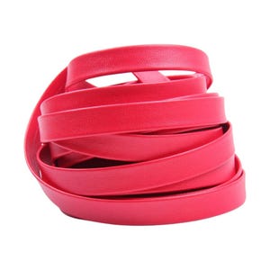 May include: A coiled length of bright red leather strap. The strap is smooth and appears to be made of a single piece of material. The edges are rounded, and the strap is tightly wound, creating a compact, circular shape. The background is plain white.