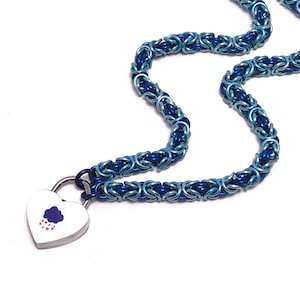 May include: A blue chainmail necklace with a heart-shaped pendant. The necklace is made of interlocking blue rings, with a lighter blue hue in the center. The heart pendant is white with a purple cloud and red hearts design.