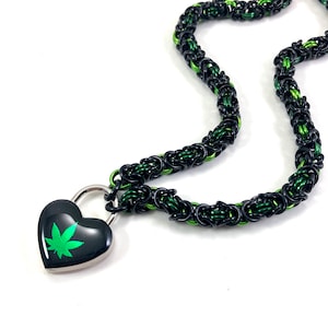 Op de afbeelding: Een zwarte en groene ketting met een hartvormig hangslot met een groen marihuanabladontwerp.